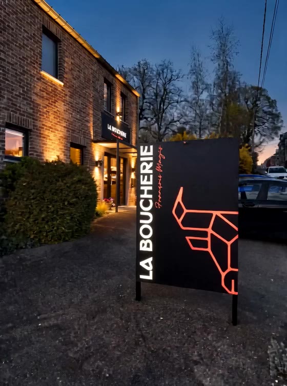Enseigne lumineuse orange La Boucherie devant une façade en briques, à la tombée de la nuit.