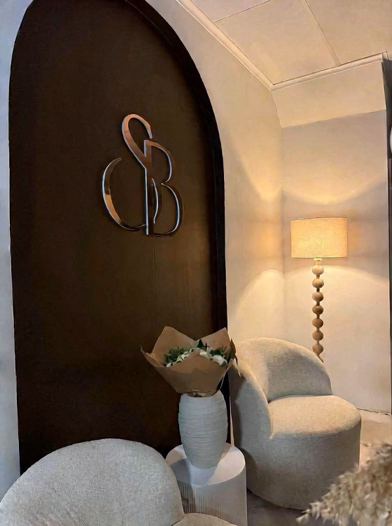 Logo SB Hair doré appliqué sur une arche murale, dans un salon aux tons chauds.